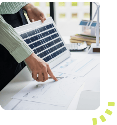 A person holding a small solar panel and pointing to paperwork